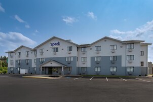 Un hotel de varios pisos con un letrero de 'Spark by Hilton', un estacionamiento y cielo despejado.