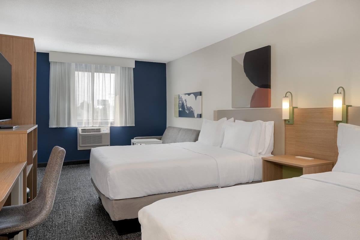 Une chambre d’hôtel avec deux lits, un bureau, une chaise et une fenêtre avec des rideaux.