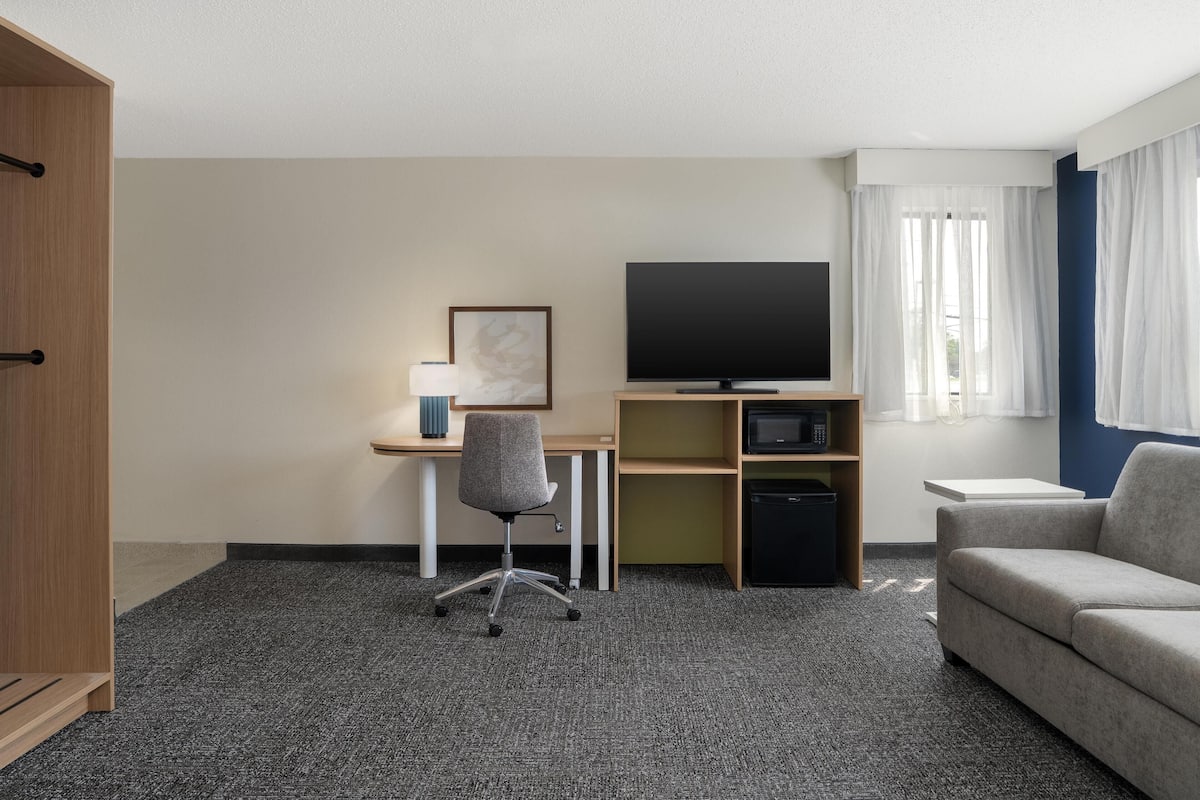 Une chambre d’hôtel équipée d’un bureau, d’une chaise, d’une télévision, d’un canapé et d’une armoire.