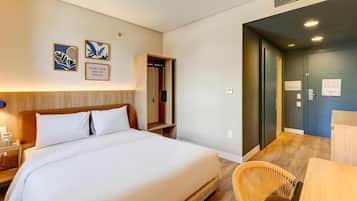 Quarto de hotel com uma cama grande, telefone ao lado da cama, cabeceira de madeira, guarda-roupa, escrivaninha e uma cadeira.