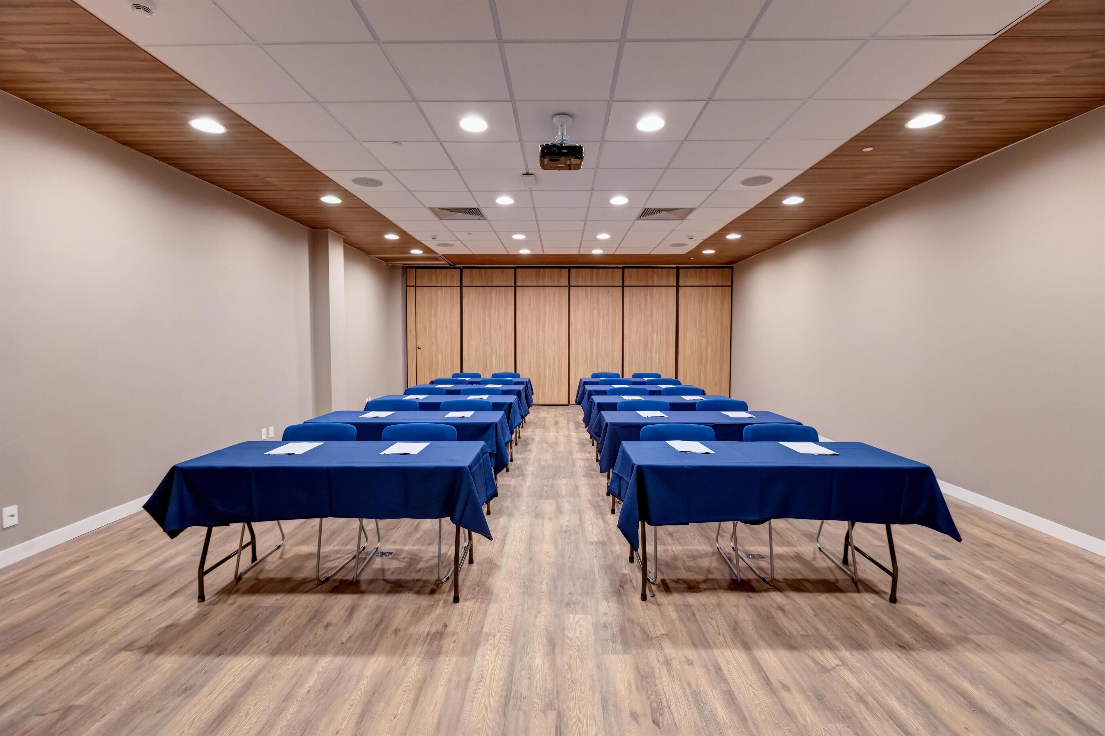 A conference room with rows of tables, a projector, and a wooden ceiling.