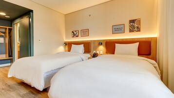 Quarto de hotel com duas camas, cabeceira de madeira, luminárias de cabeceira e quadros nas paredes.
