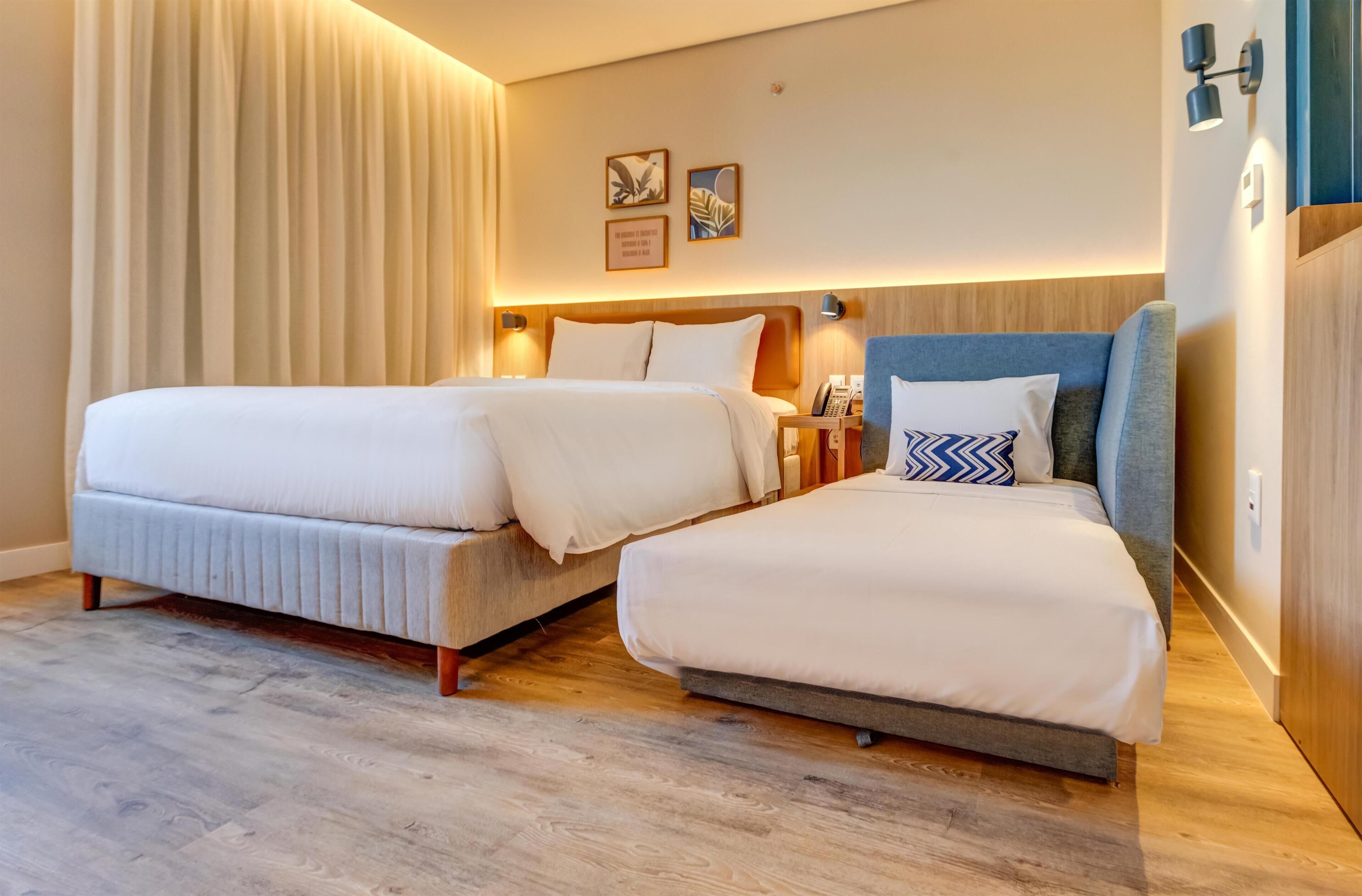 Een hotelkamer met twee bedden, houten vloeren en een wandlamp.