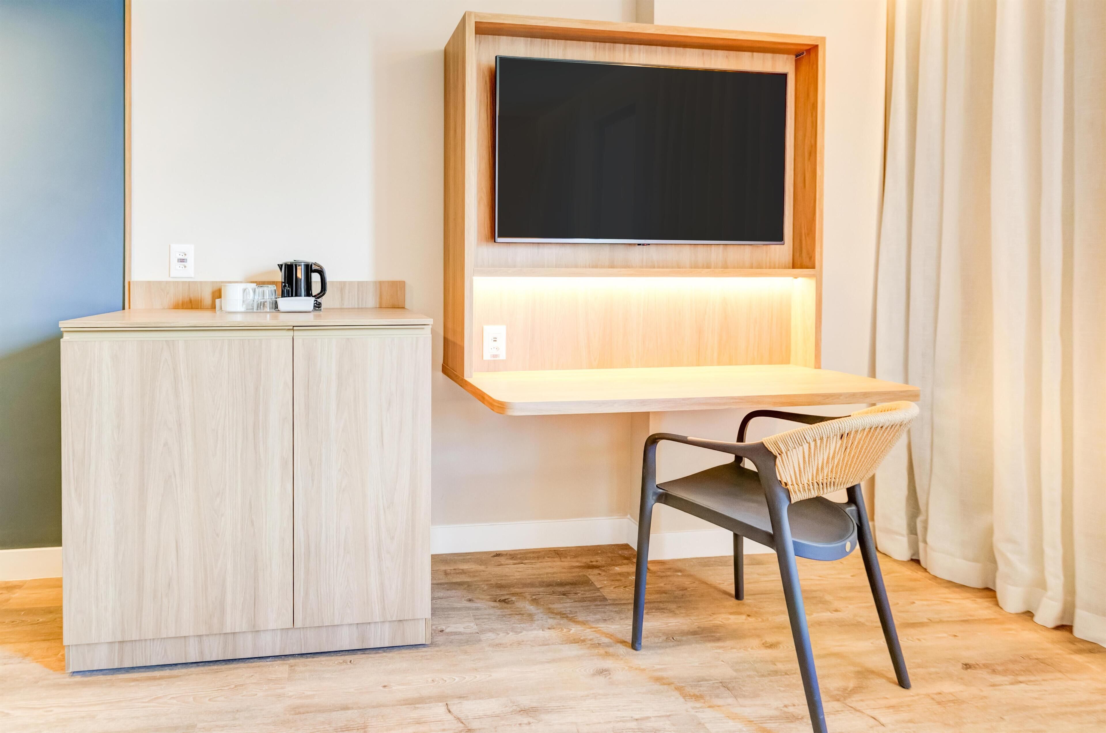 Una habitación compacta con un escritorio de madera, una silla, un televisor de pantalla plana y un mueble pequeño.