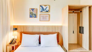 Quarto de hotel com uma cama, um telefone ao lado e um painel de cabeceira de madeira.
