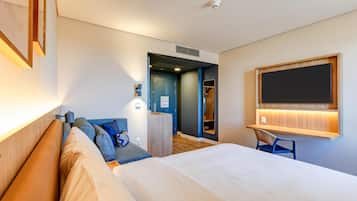 Habitación de hotel con una cama grande, un escritorio con una silla, un armario y un baño visible a través de una puerta abierta.