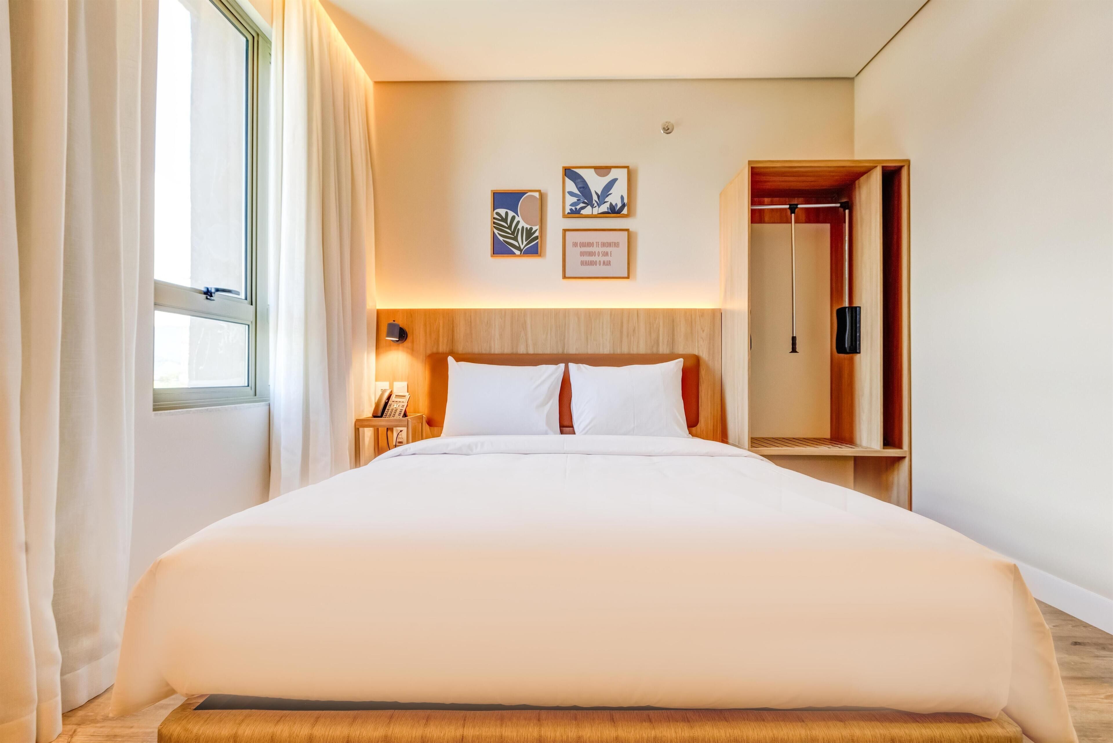 Una habitación de hotel con una cama grande, una mesita de noche con lámpara y un armario.