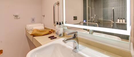 A modern bathroom with a large mirror, a white sink, and a towel rack.