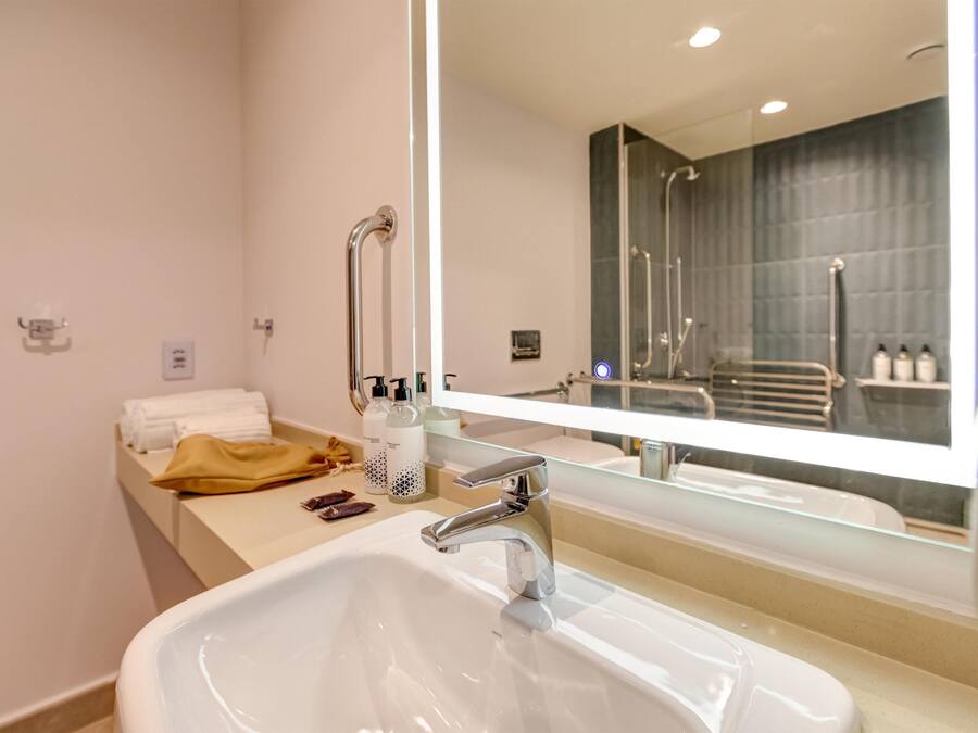 A modern bathroom with a large mirror, a white sink, and a towel rack.