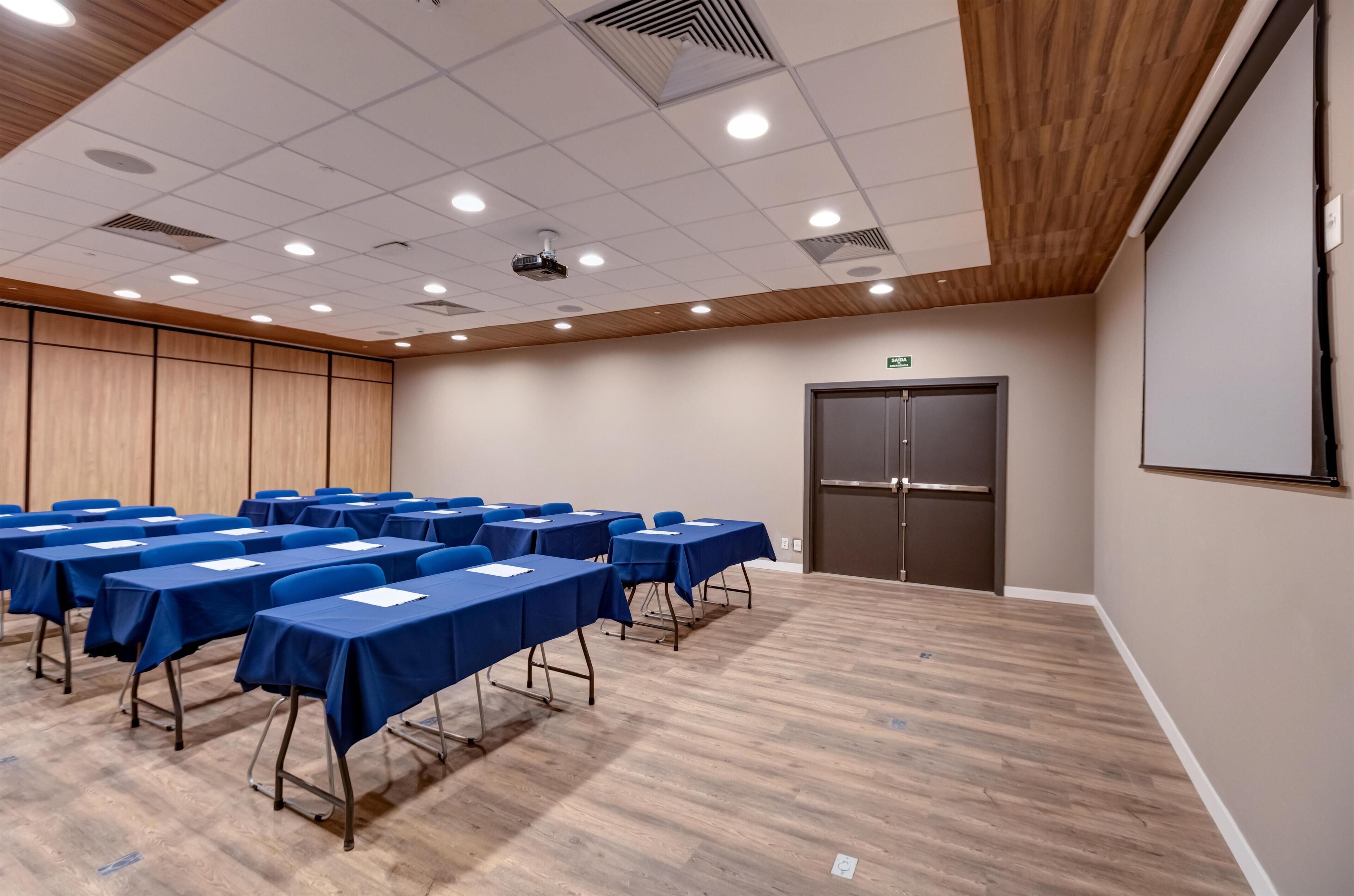 Un salón de conferencias con varias mesas y sillas, un proyector y una puerta.
