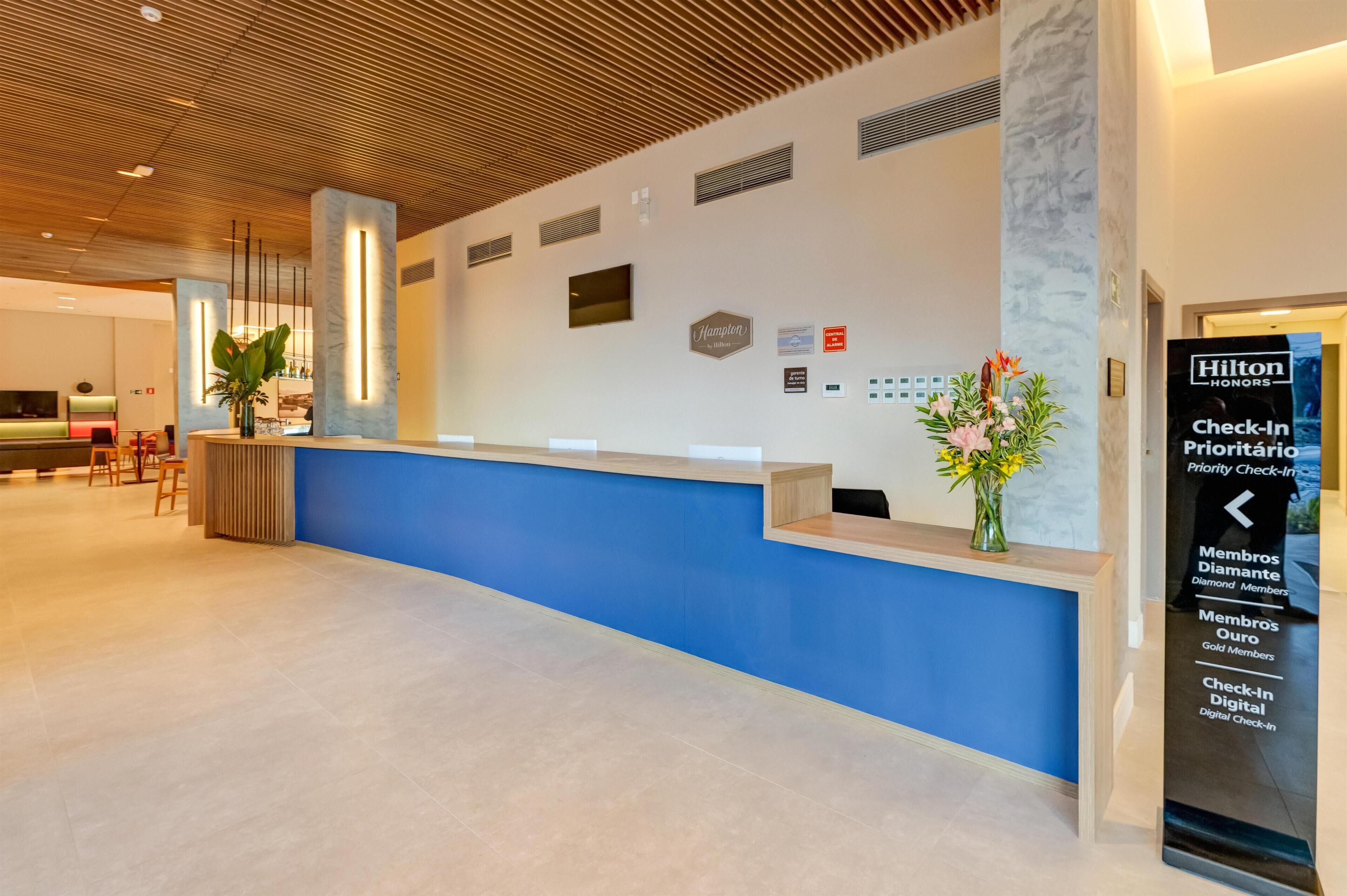 Een hotel receptie met een blauw aanrecht, een houten plafond en een bord met de tekst 'Inchecken voor Hilton Honors leden'.