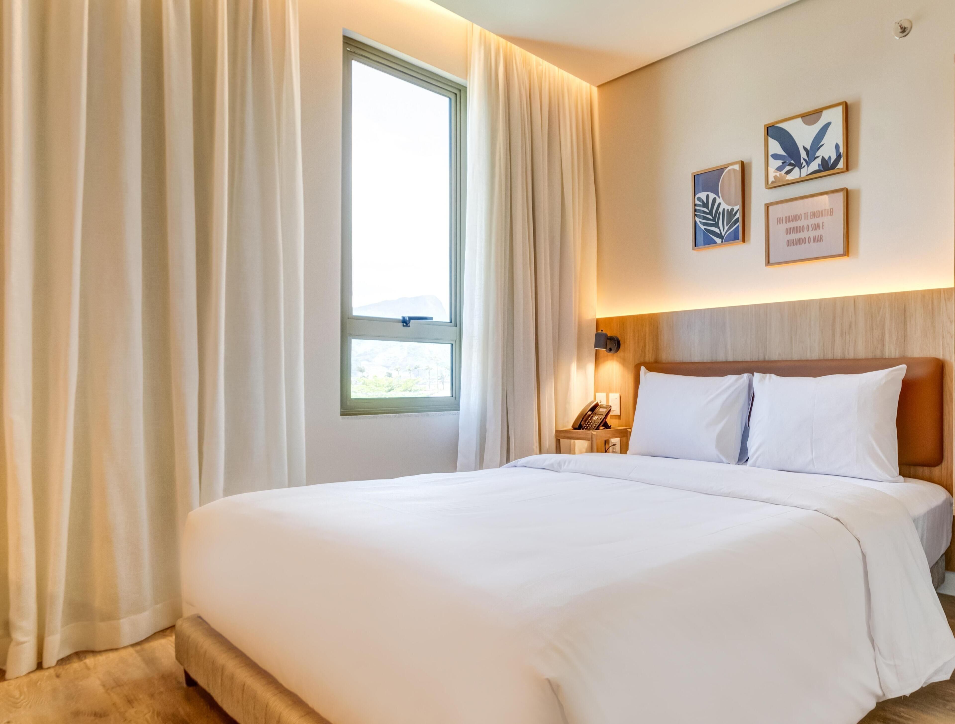 A hotel room with a large bed, a bedside table with a lamp, and a window with curtains.
