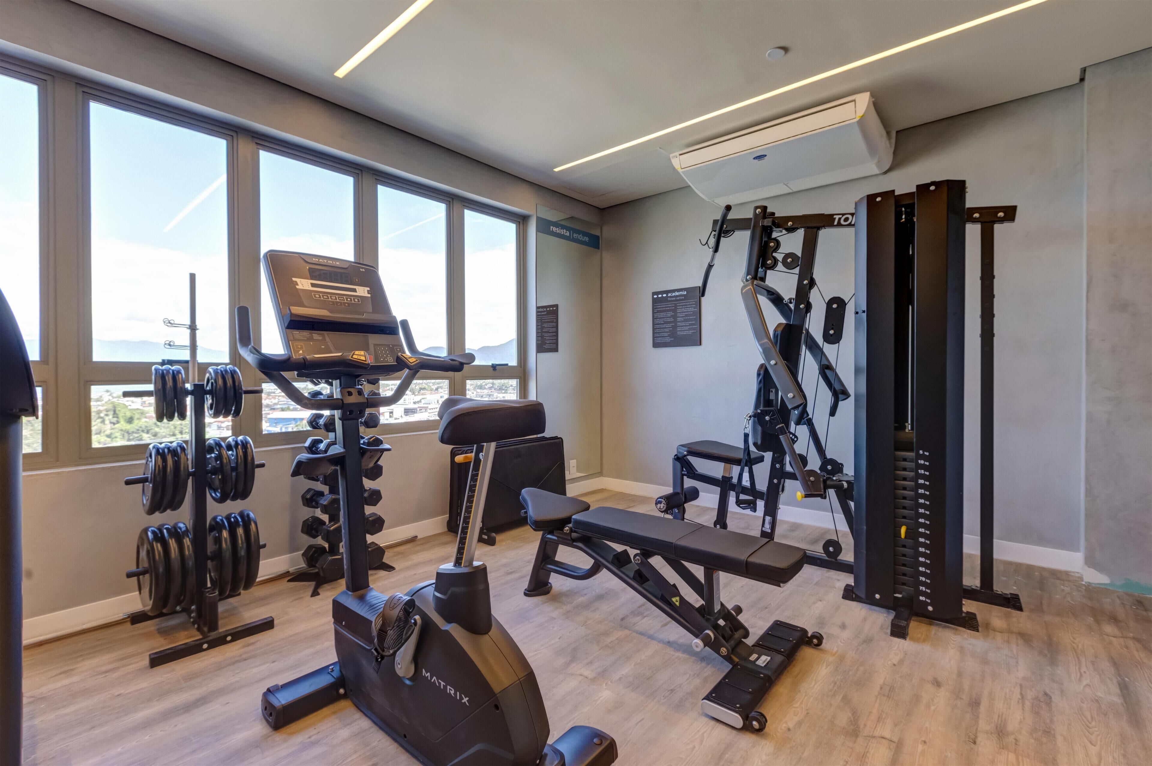Une salle de sport équipée de machines de cardio, de postes d’entraînement en musculation et d’un banc de développé couché.