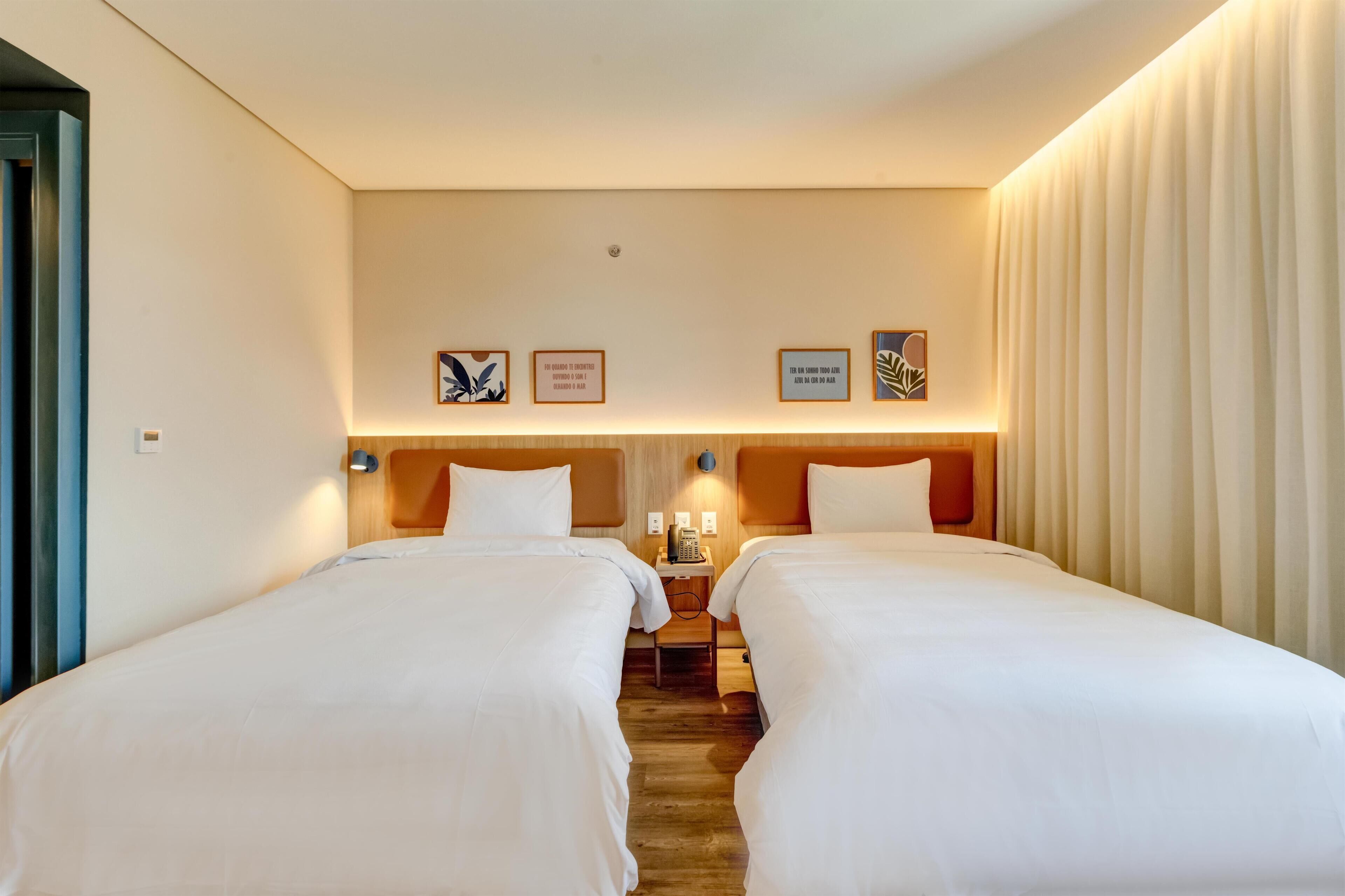 A hotel room with two beds, a nightstand with a phone, and framed quotes on the wall.