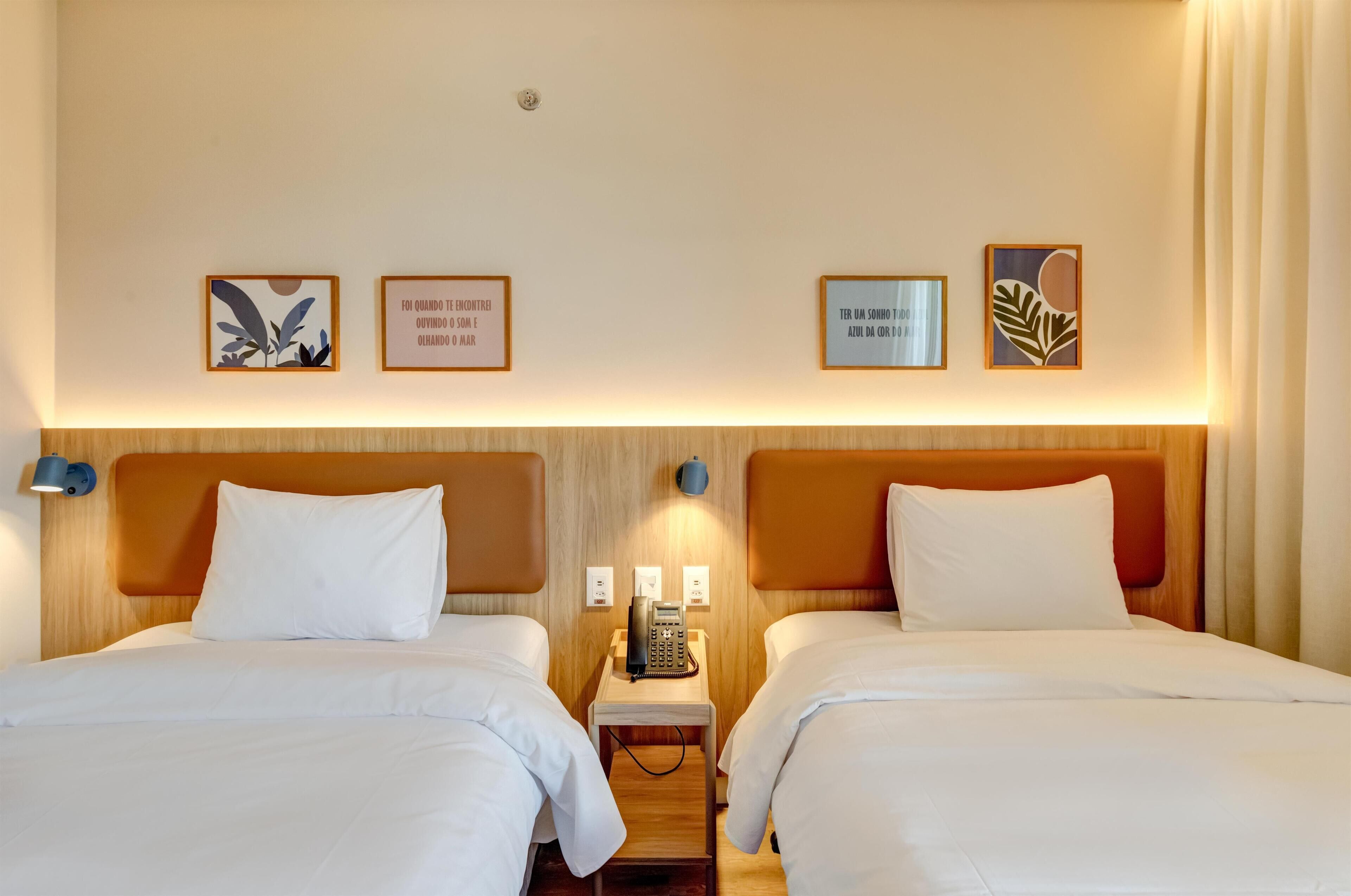 Camera d'albergo con due letti, un comodino con il telefono e opere d'arte alle pareti.