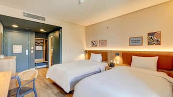 Une chambre d’hôtel avec deux lits, un bureau et une chaise. Un placard et un miroir se trouvent sur un des murs.
