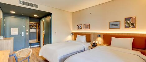 A hotel room with two beds, a desk, and a chair. There is a wardrobe and a mirror on one wall.