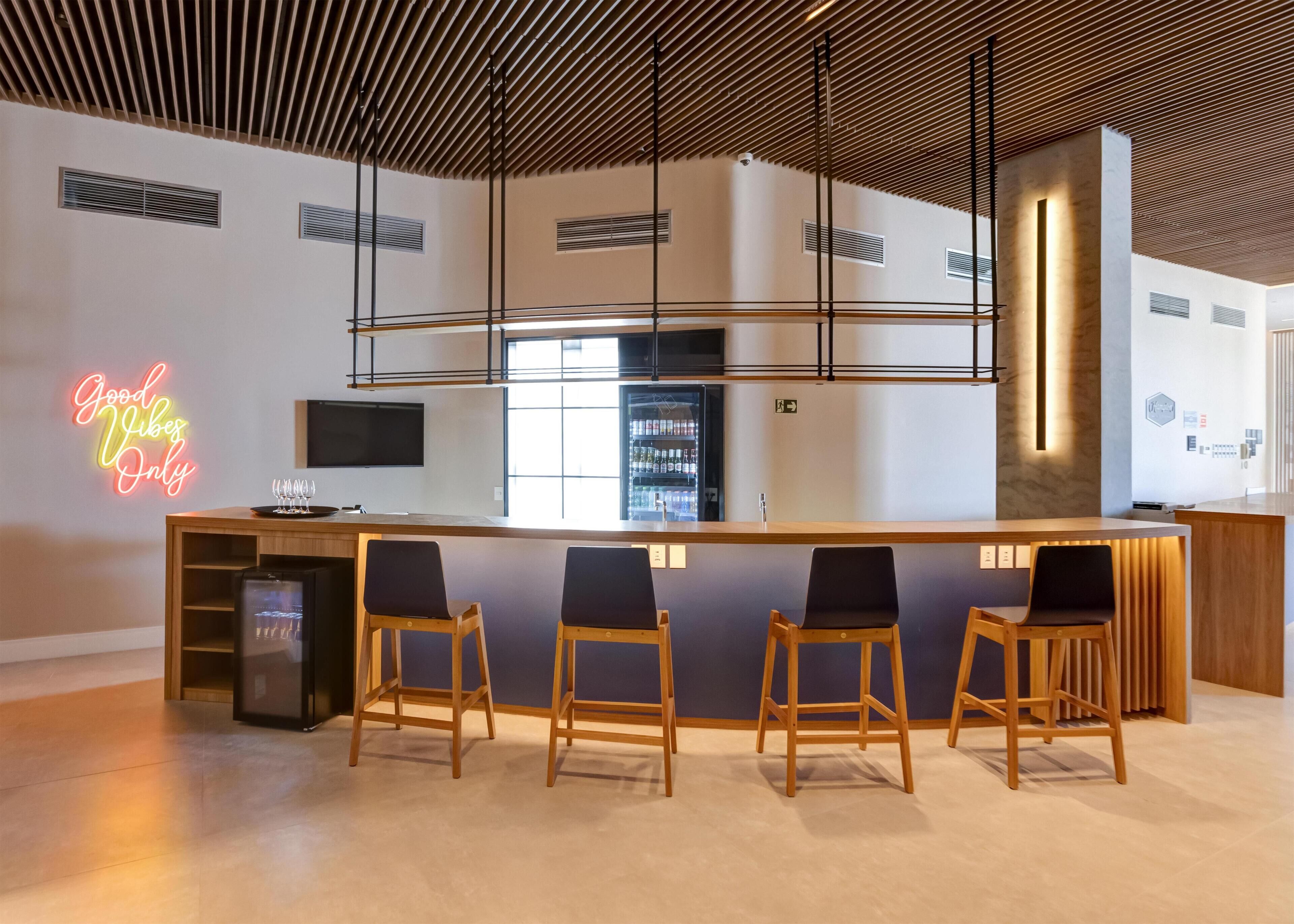 A modern bar area with a neon sign, wooden bar counter, and four bar stools.