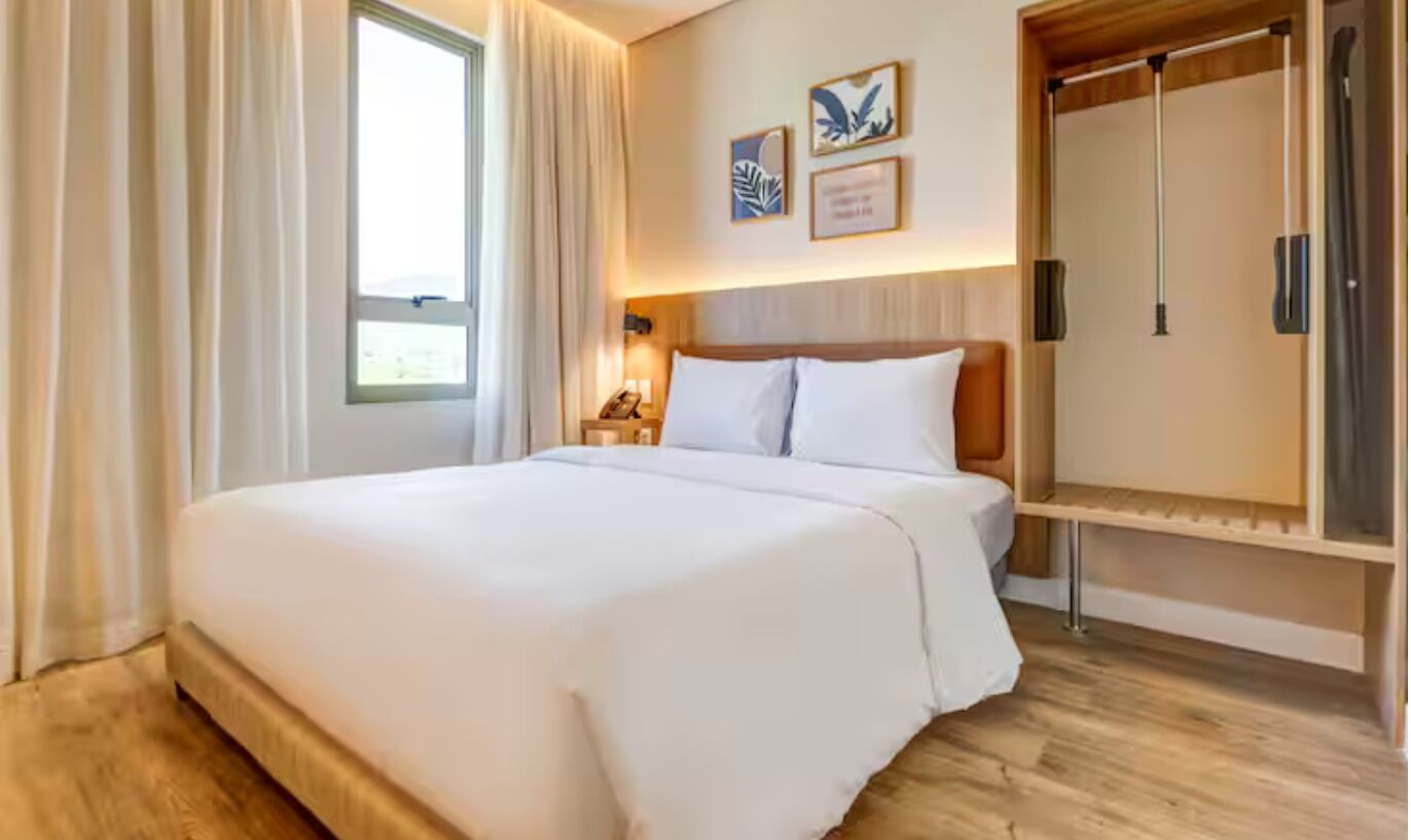 Une chambre d’hôtel avec un grand lit, une armoire, une table de chevet avec une lampe et une fenêtre avec des rideaux.