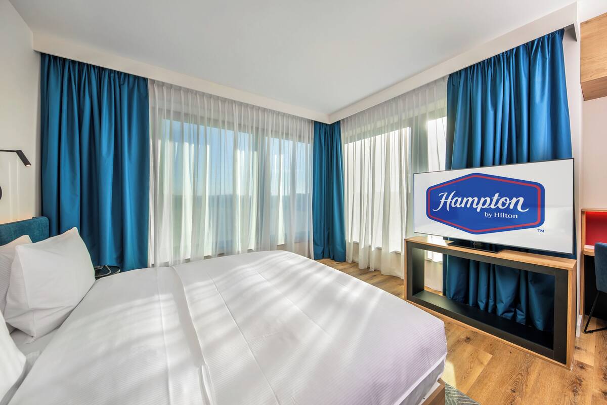 Ett hotellrum med en säng, en platt-TV, ett skrivbord och en stol.