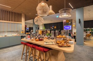 Un bar à petit-déjeuner moderne, doté de sièges, proposant une variété d’aliments et arborant une enseigne Hampton by Hilton.