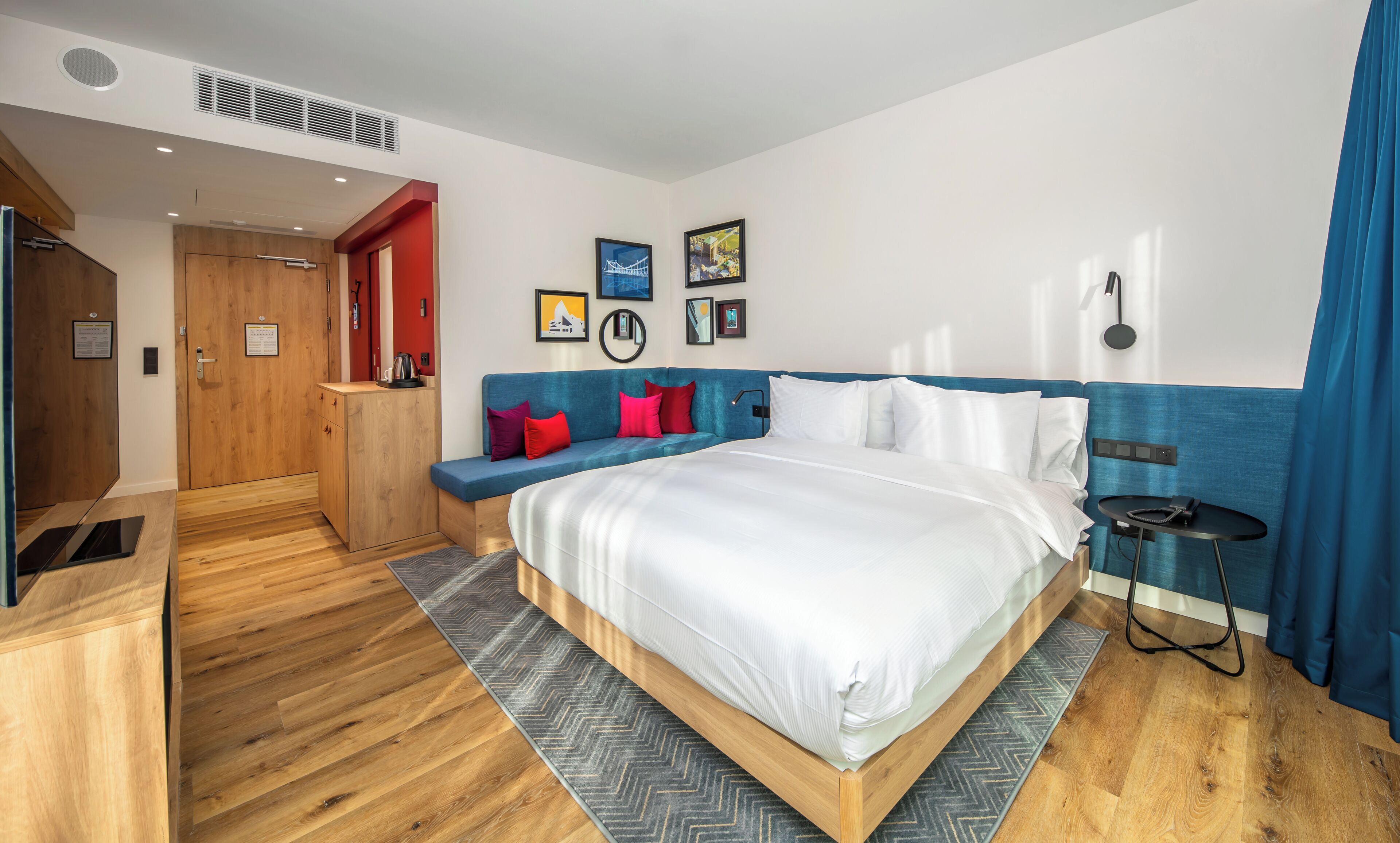 Une chambre d’hôtel moderne dotée d’un grand lit, d’un coin salon avec des coussins, d’une petite table et d’une lampe fixée au mur.