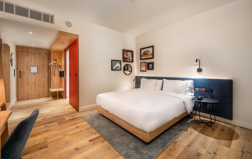 Une chambre d’hôtel moderne équipée d’un grand lit, d’un bureau, d’une chaise, d’une petite table et d’une armoire.