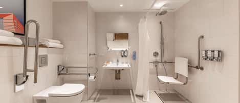 A modern bathroom with a toilet, sink, and shower. It includes grab bars and a hand dryer.