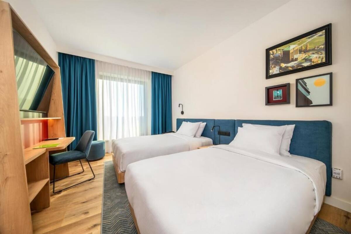 Ett hotellrum med två sängar, ett skrivbord, en stol och konstverk på väggen.