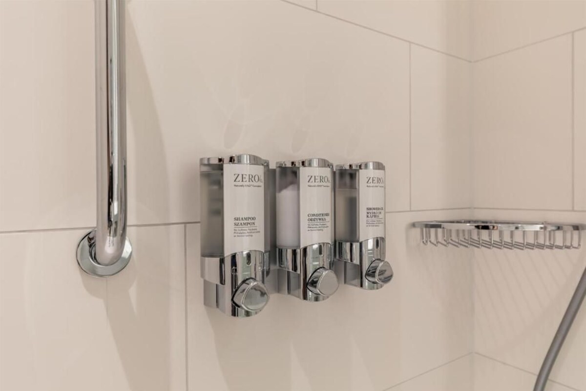 A bathroom with four ZERO shampoo dispensers mounted on the wall, a chrome showerhead, and a chrome towel rack.