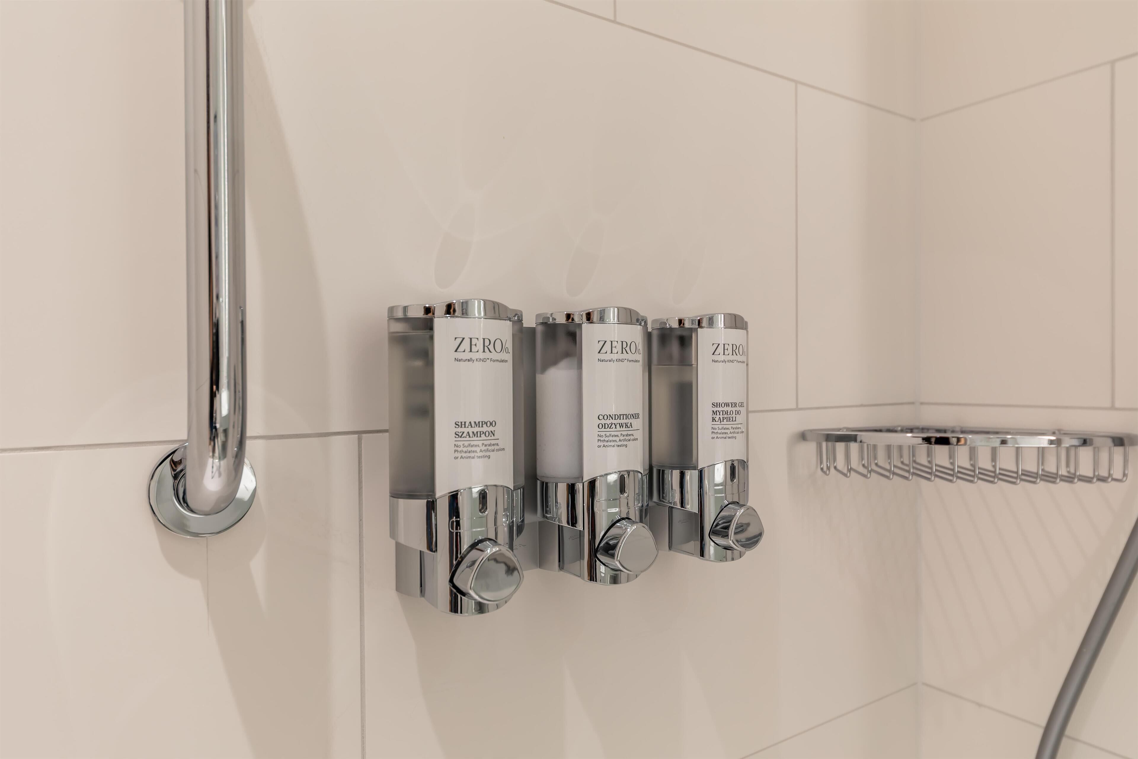 Un baño con cabezal de ducha cromado, toallero cromado y tres botellas de champú y acondicionador.
