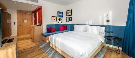 Habitación de hotel moderna con una cama grande, un rincón de estar con cojines rojos, piso de madera y una pared azul decorativa.