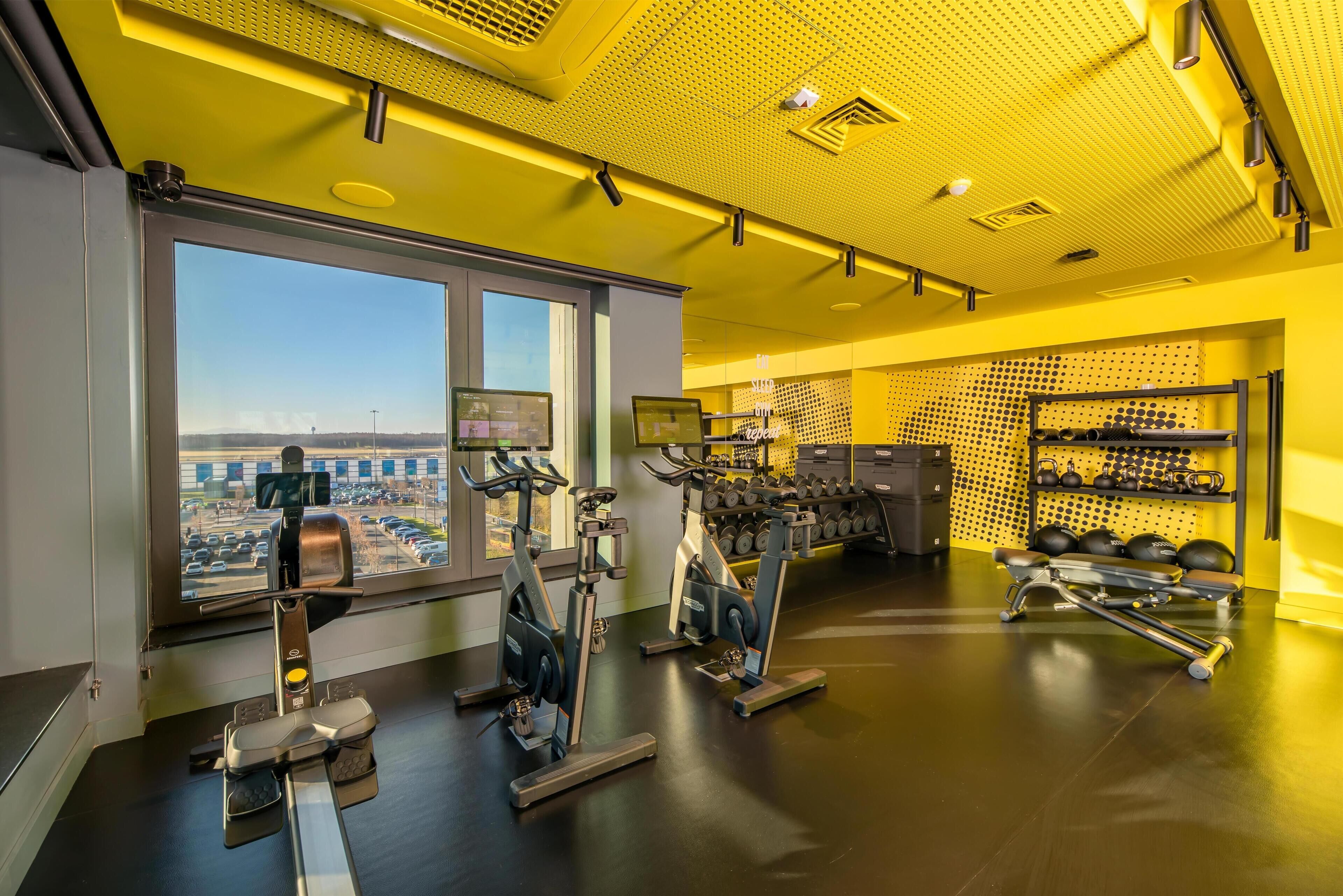 A gym with exercise equipment, a large window, and a view of a parking lot.