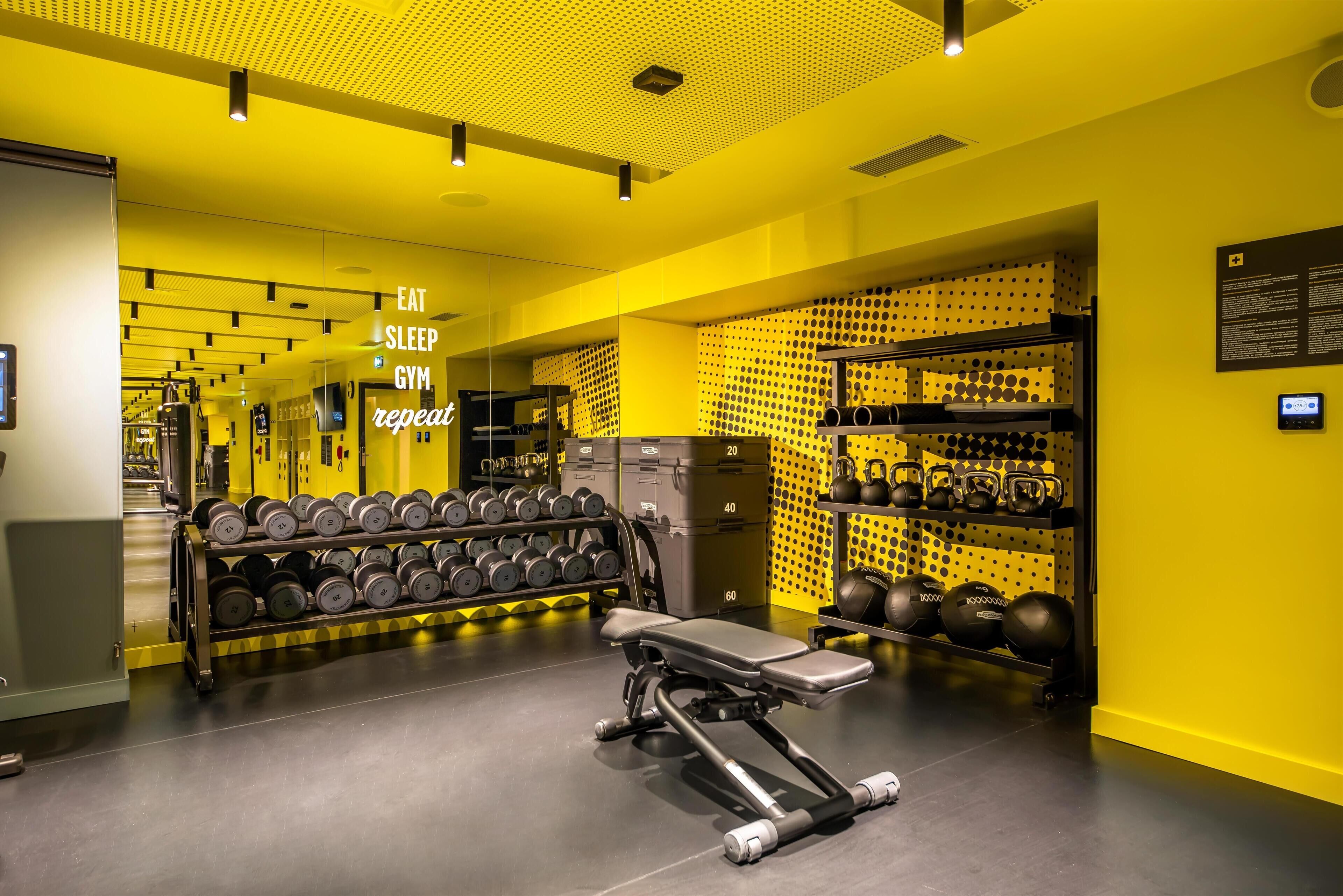 A gym with a mirrored wall, weight racks, and a bench press.