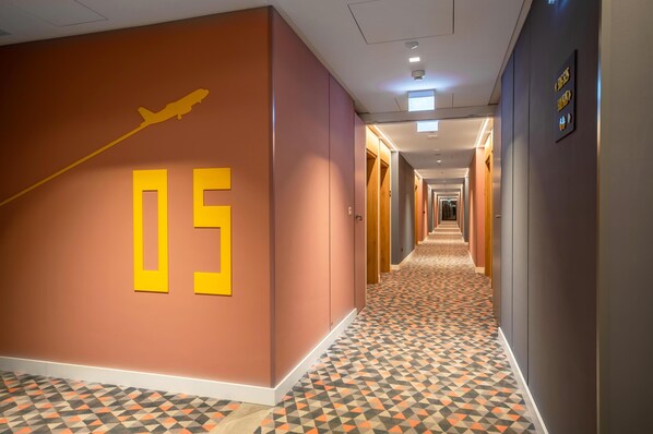 Pasillo de hotel con piso de diseño geométrico, el número '05' grande en la pared y una silueta de escaleras.