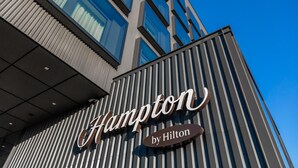 Une enseigne d’hôtel portant le nom « Hampton by Hilton » sur la façade d’un immeuble moderne.