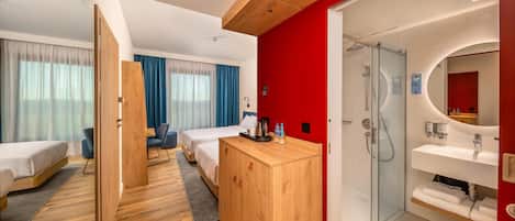 Habitación de hotel con dos camas, un armario de madera, un escritorio, una silla, zona de ducha y baño con espejo y lavabo.