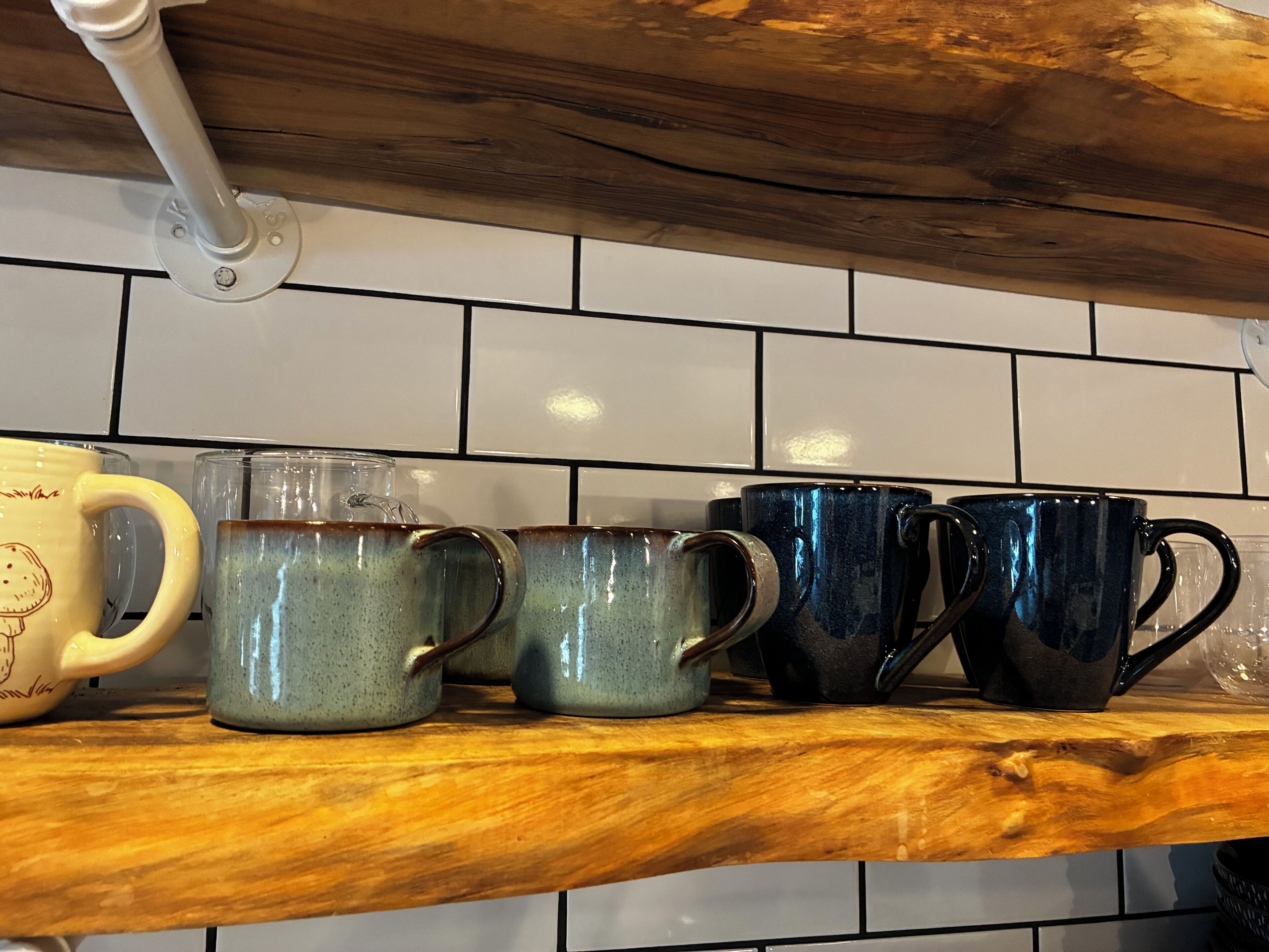 Une étagère de cuisine avec différentes tasses en céramique et un pichet en verre.