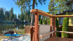A wooden deck with a hot tub, a kayak, and a paddleboard near a lake.