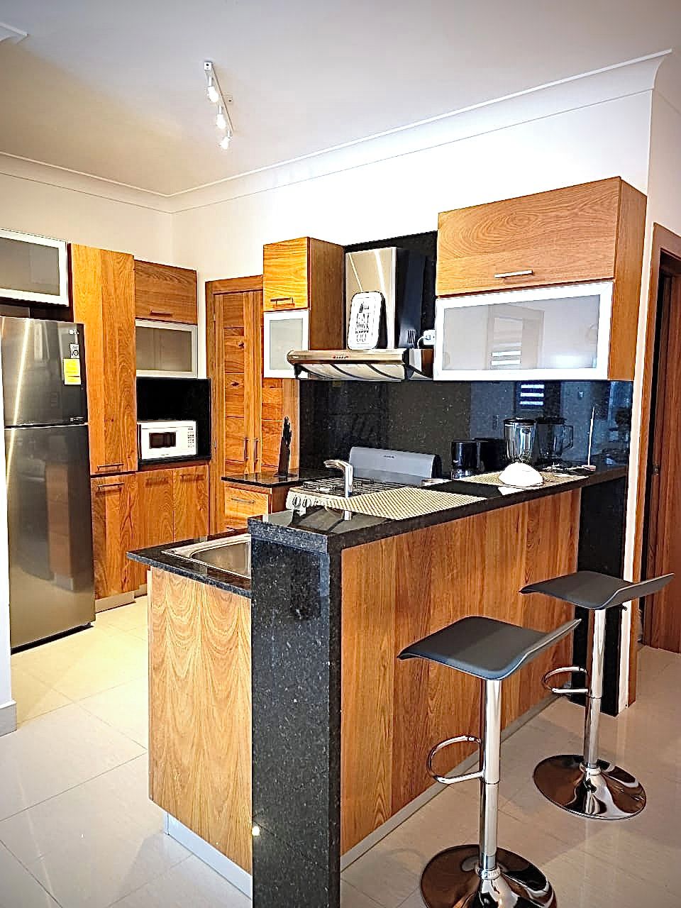 A modern kitchen with wooden cabinets, stainless steel appliances, a central island, and bar stools.
