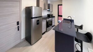 A modern kitchen with stainless steel appliances, a black countertop, and a black chair.