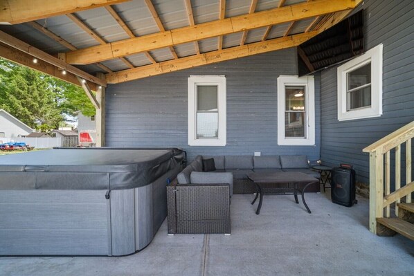 An outdoor patio with a hot tub, seating area, and a staircase leading to a covered deck.