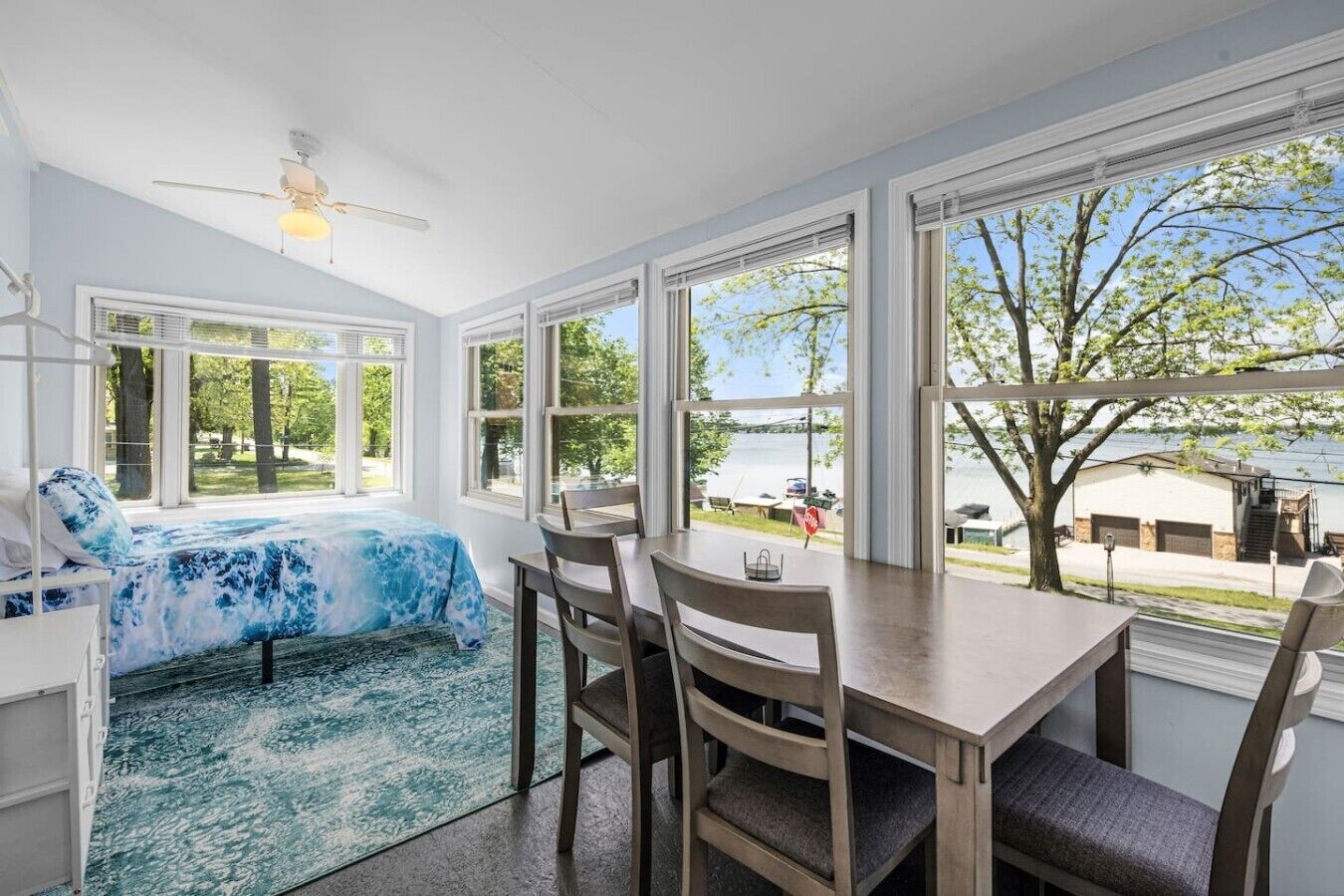 Une pièce comprenant un lit, une table à manger et des chaises. De grandes fenêtres offrent une vue sur l’extérieur.