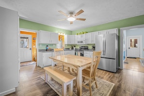 A kitchen with white cabinets, a wooden dining table, and a ceiling fan.