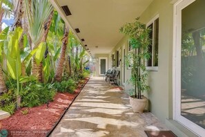 Un pasillo cubierto con suelo de concreto, rodeado de exuberante vegetación tropical y un árbol en maceta.