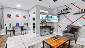 Een moderne woonkamer met een eethoek, een aan de muur bevestigde televisie en een plafondventilator.