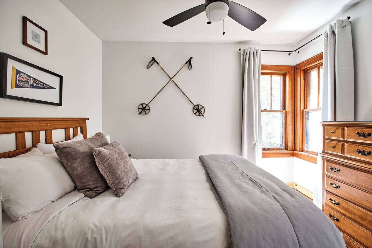 Camera da letto con un letto, una testiera in legno, una ventola a soffitto, un elemento decorativo a parete e una finestra con tende.