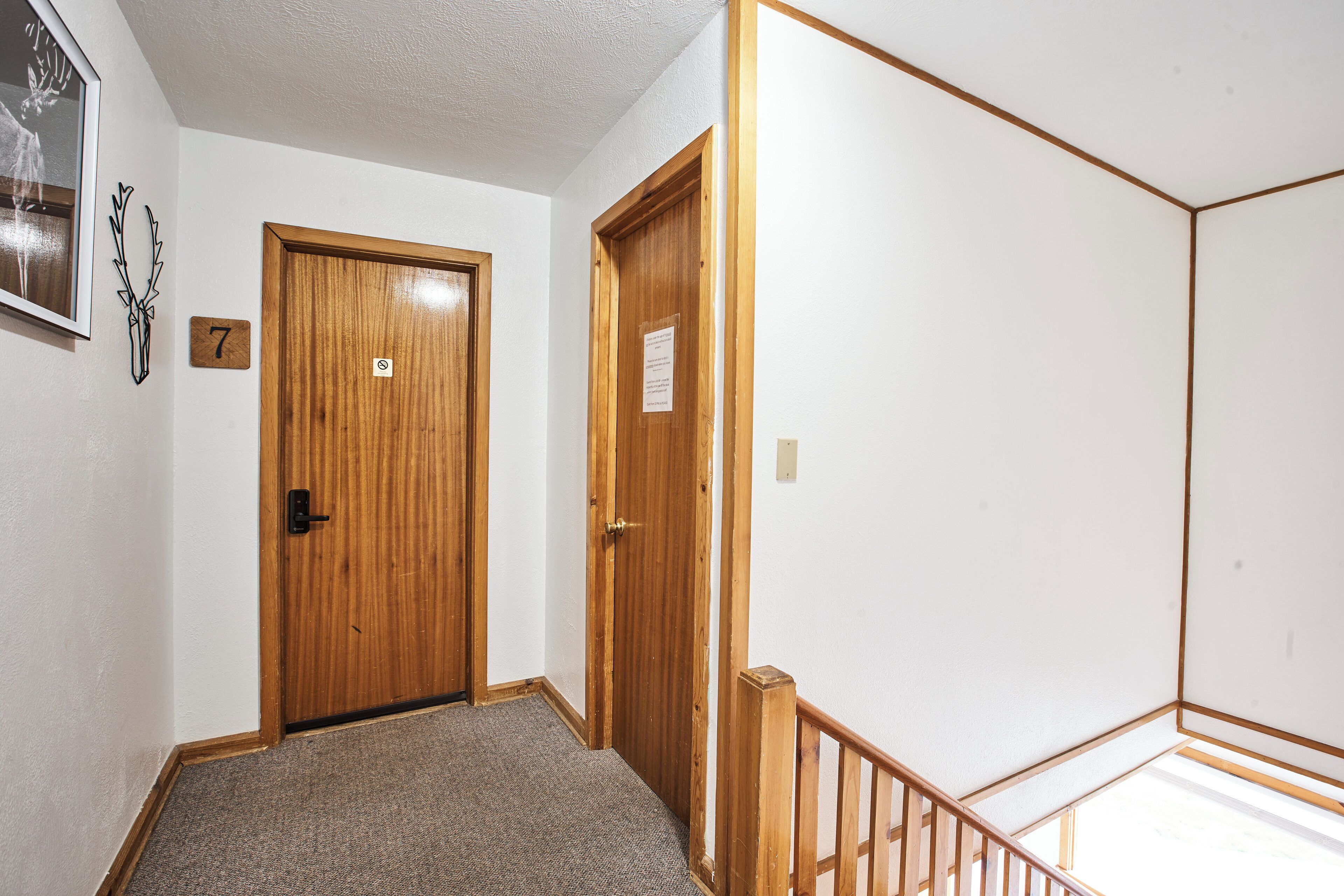 A hallway with two wooden doors, a carpeted floor, and a wooden railing.
