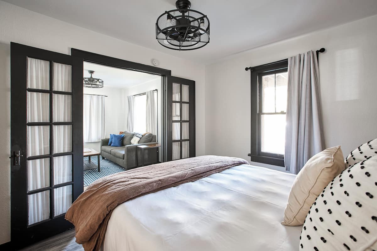 Una camera da letto con un letto, uno specchio grande e vista su un'altra stanza attraverso una porta aperta.
