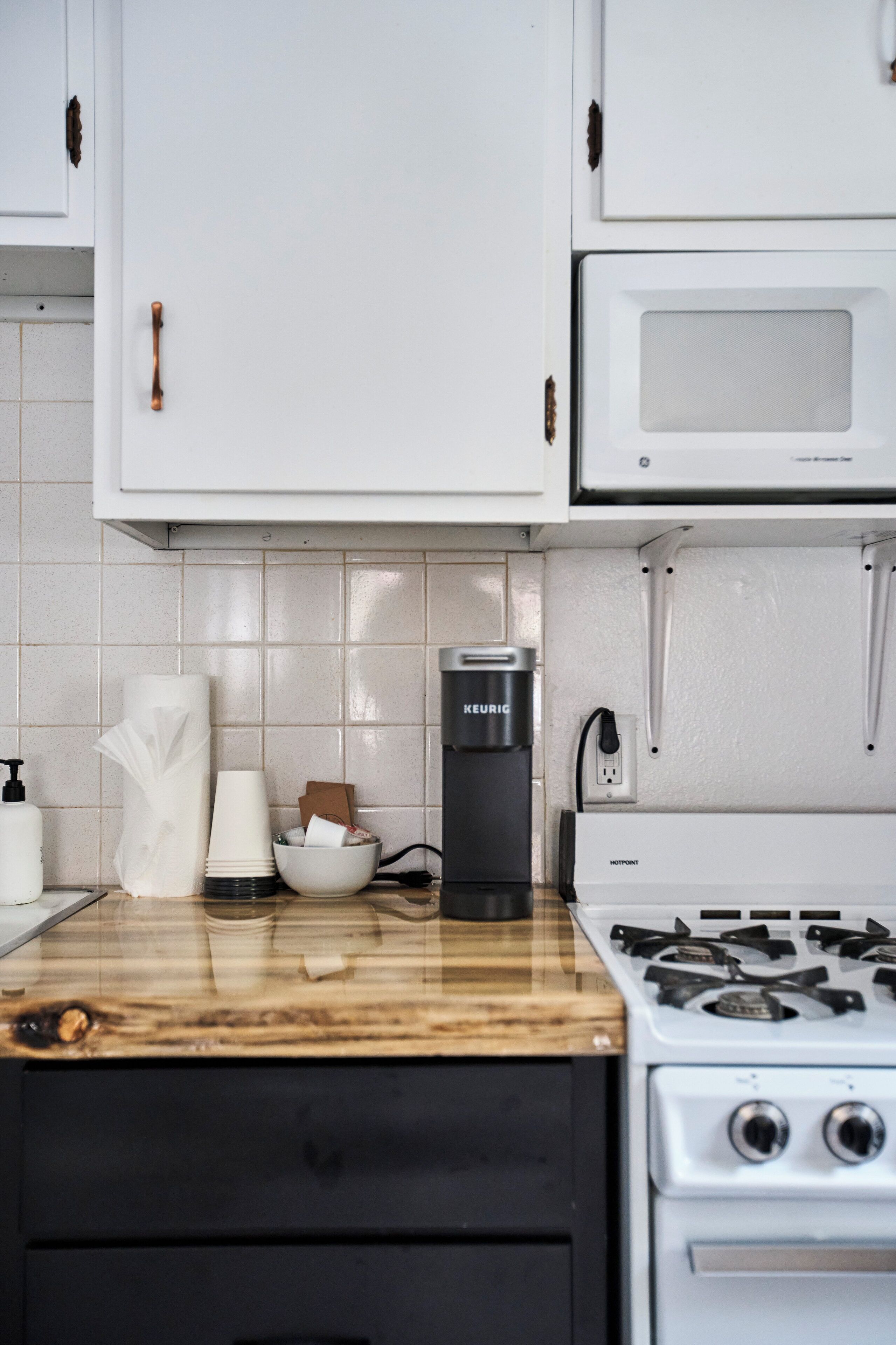 A kitchen with white cabinets, a microwave, a Keurig coffee maker, a gas stove, and a wooden countertop.